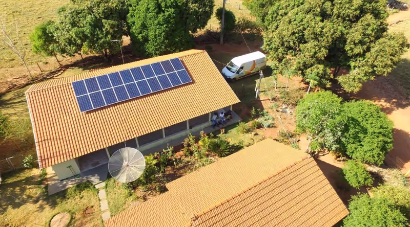 Vista aérea de casa de fazenda com painéis solares no telhado, cercada por árvores
