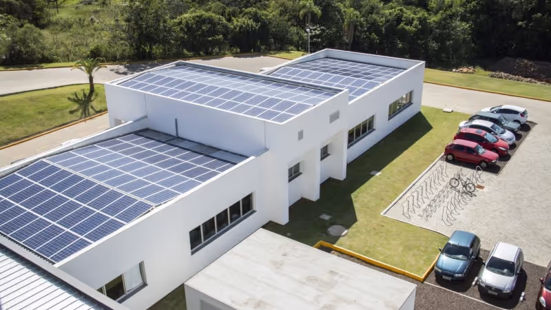 Vista aérea de prédio comercial com painéis solares em todo o telhado e estacionamento ao lado
